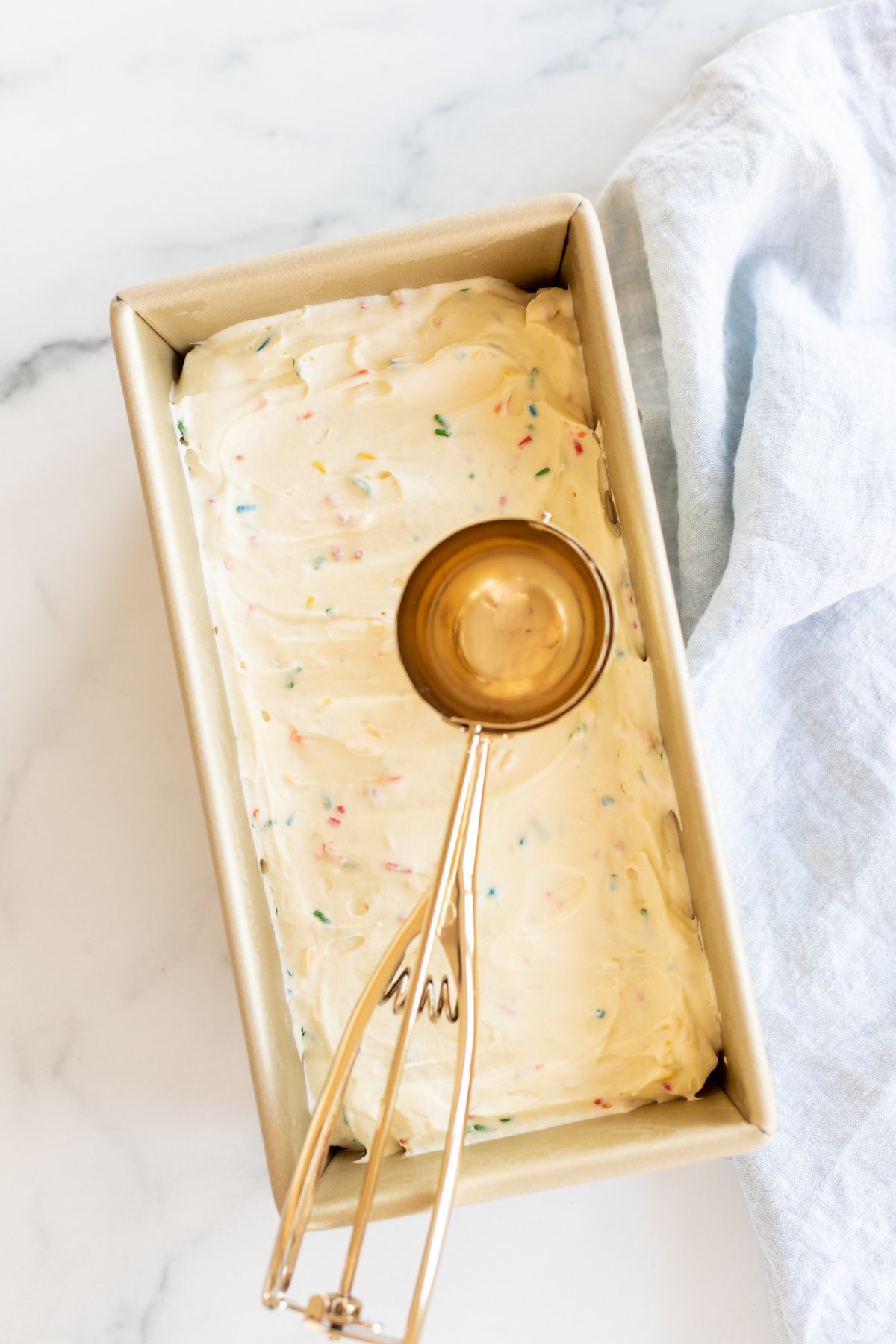 Homemade cake batter ice cream with rainbow sprinkles in a gold loaf pan.