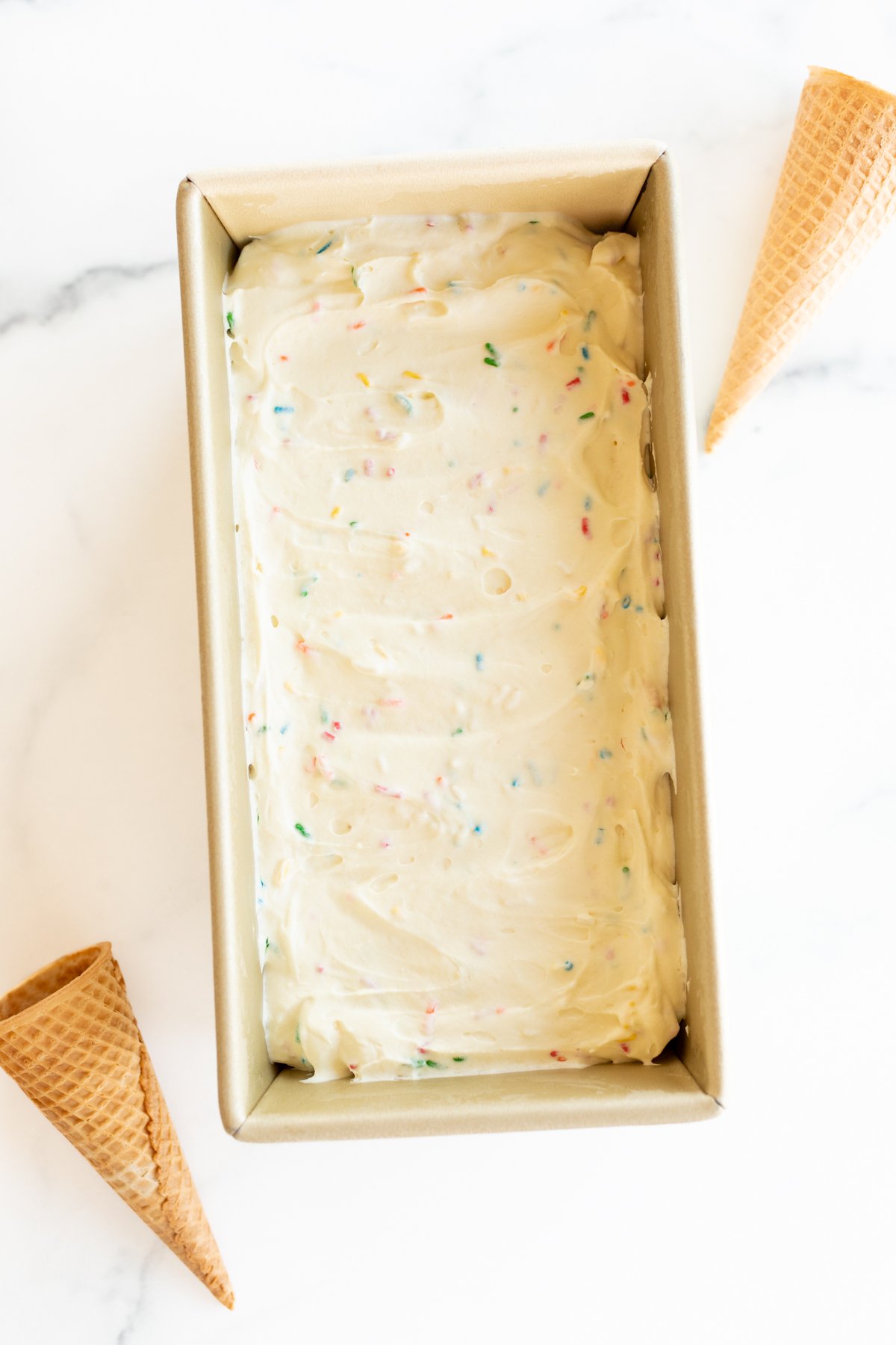 Homemade cake batter ice cream with rainbow sprinkles in a gold loaf pan.