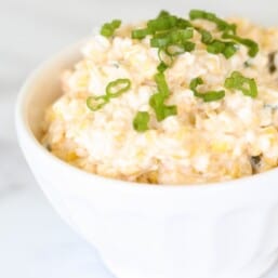 A white bowl full of fresh crack corn dip, topped with diced green onions.