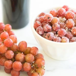 A bowl of sugared grapes with a bunch of fresh, frozen grapes to the side.