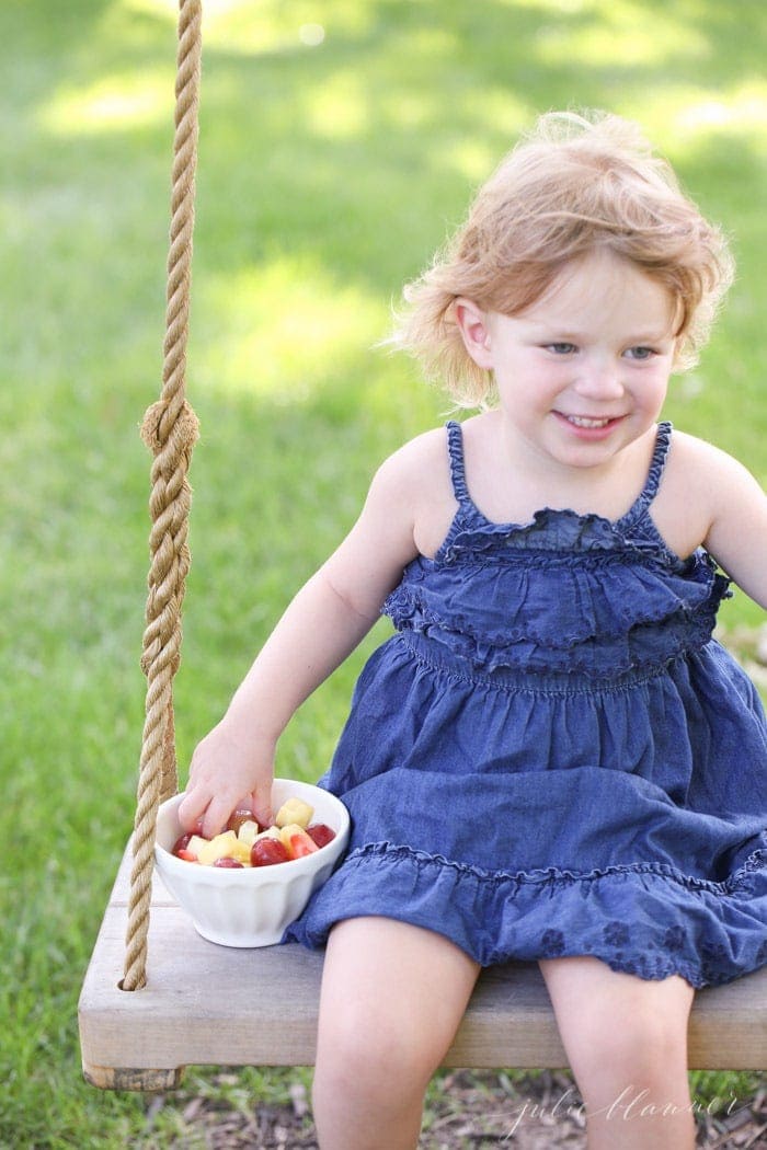 A little girl on a swing with her hand in a white bowl