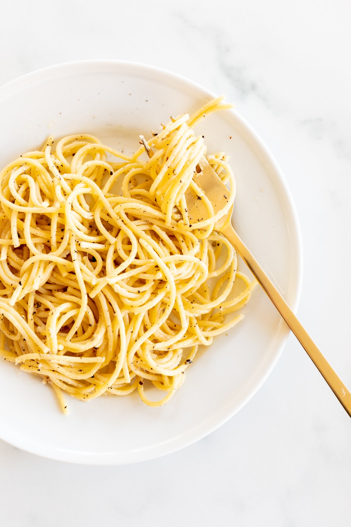 Cacio e pepe on a white plate with a gold fork.