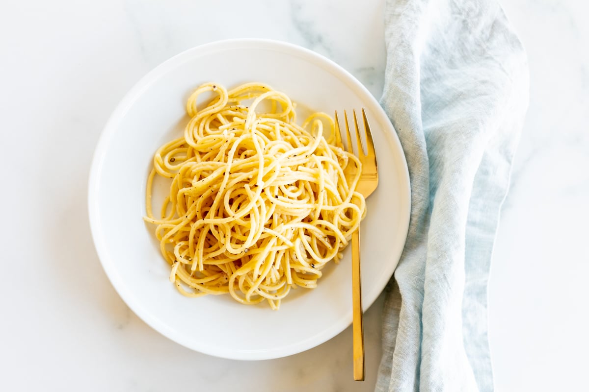 Cacio e pepe on a white plate with a gold fork.