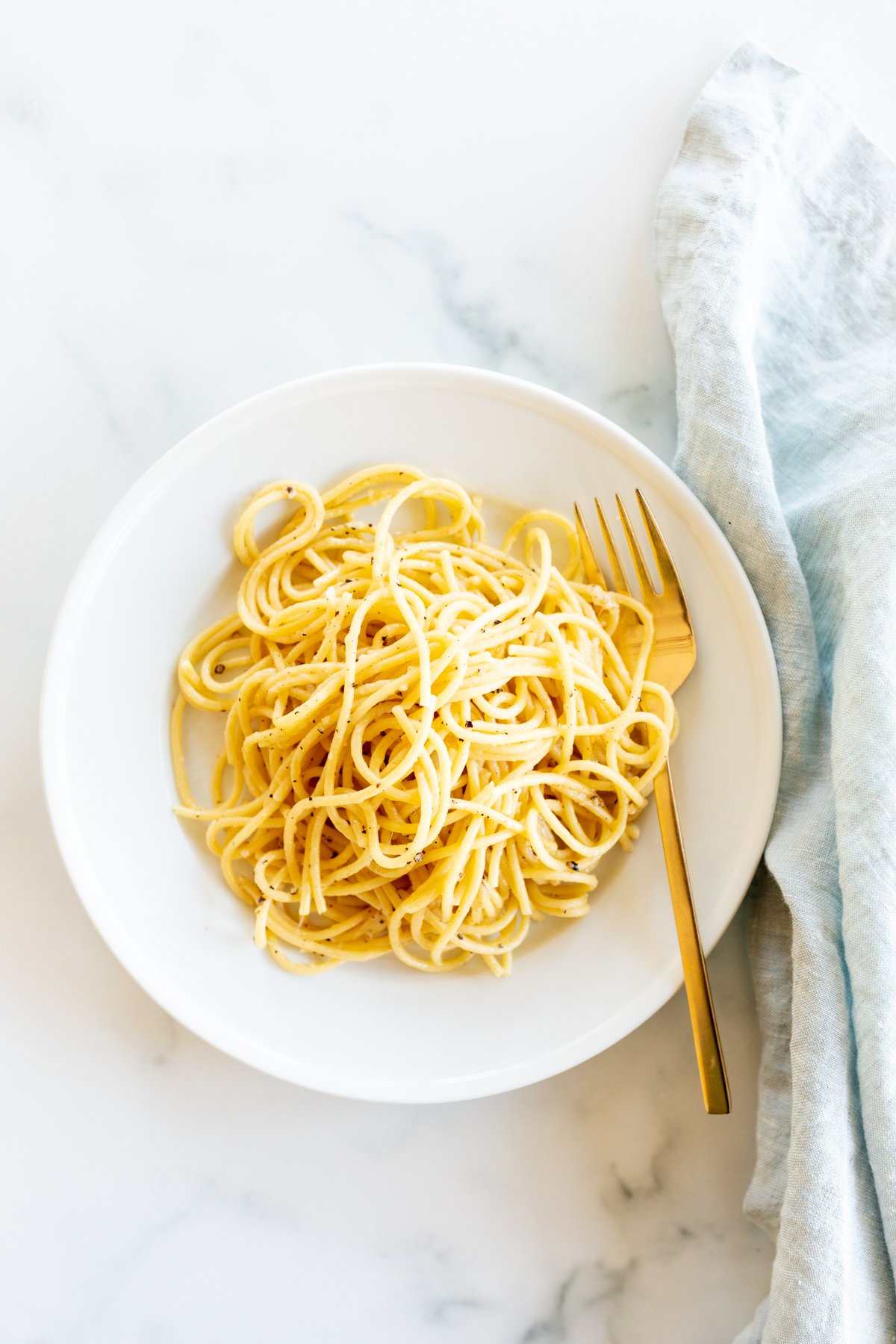 Cacio e pepe on a white plate with a gold fork.