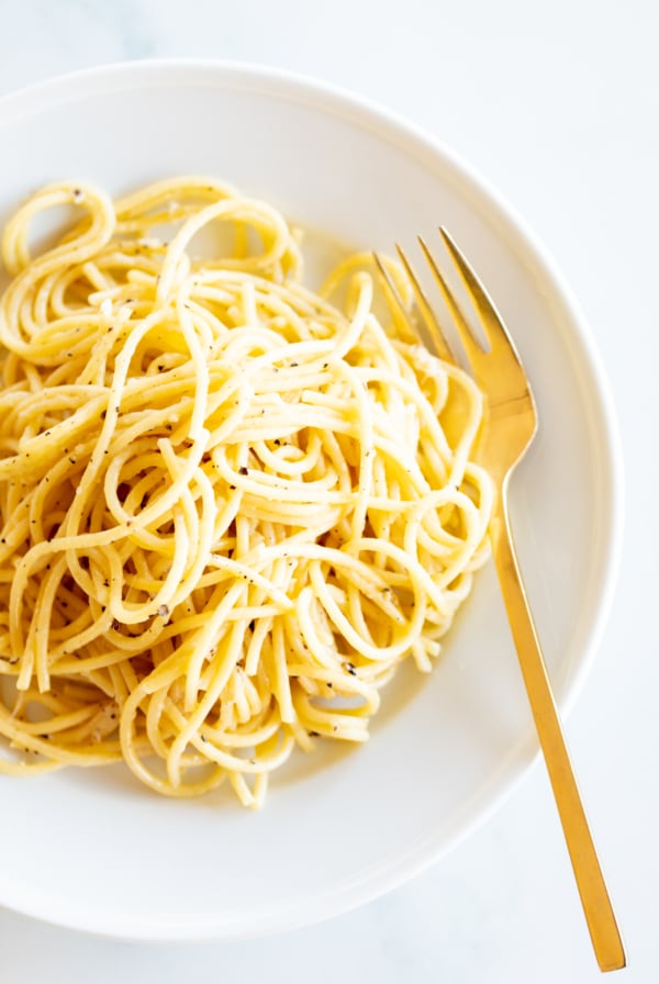 Cacio e pepe on a white plate with a gold fork.