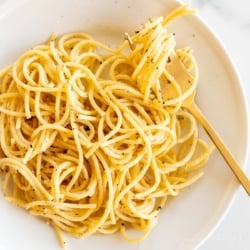 Cacio e pepe on a white plate with a gold fork.