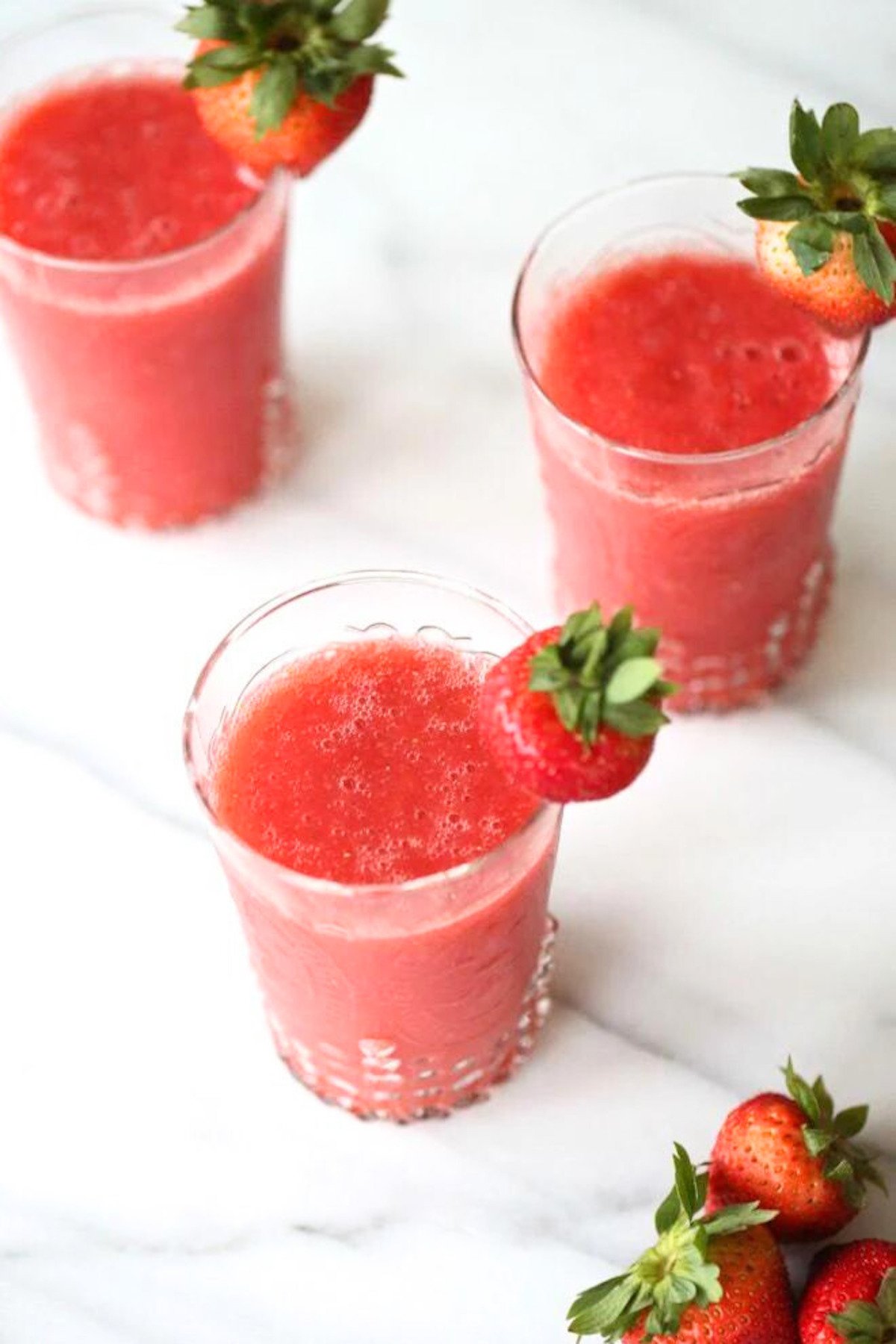 Three champagne slushies garnished with fresh strawberries