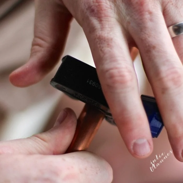 Close-up of hands using a pipe cutter tool to fix a piece of copper pipe, perfect for creating diy copper curtain rods.