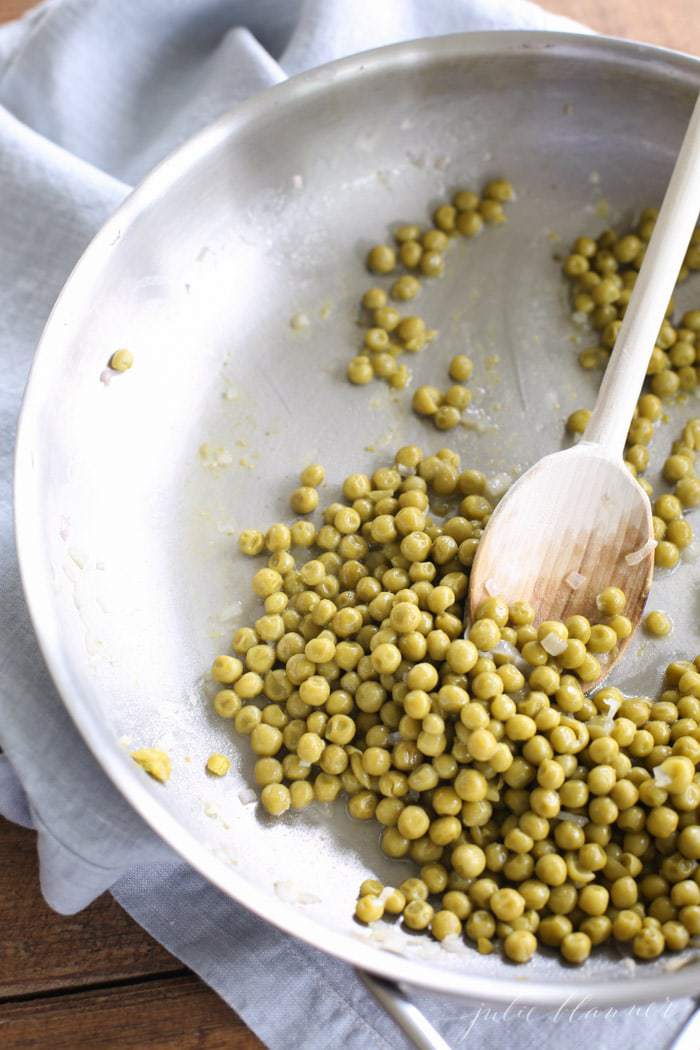 green peas in a large skillet with wooden spoon