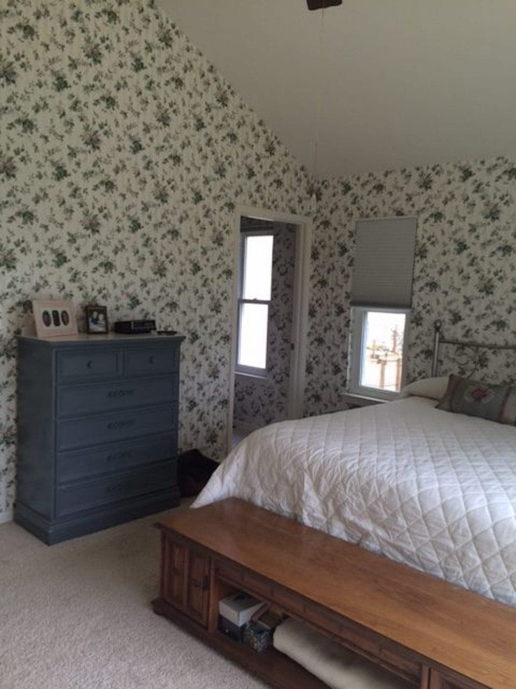 A dark bedroom with dated wallpaper on the walls and several windows.