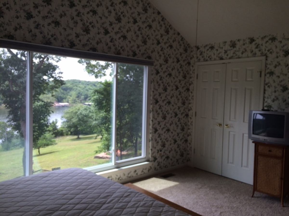 A dark bedroom with dated wallpaper on the walls and several large windows.