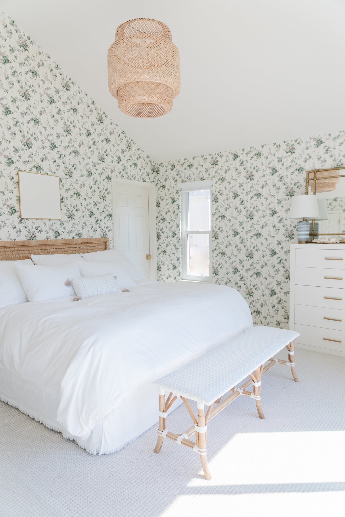 A white bed in a bedroom with [dated] floral wallpaper.