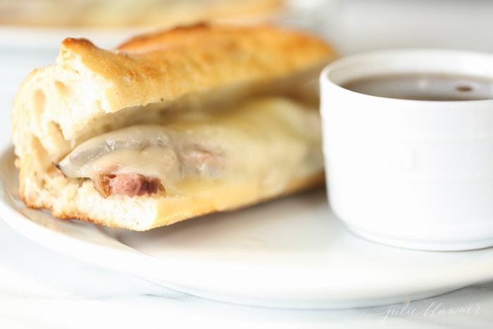 game day French dip sandwich recipe on white plate with au jus in white bowl