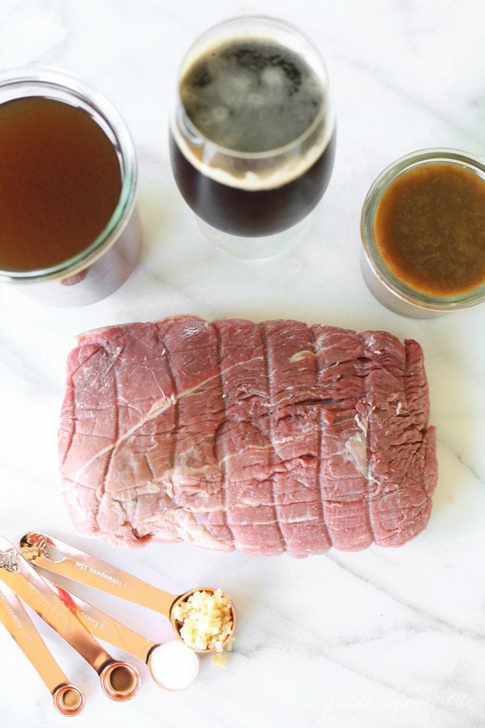 beef rump roast, measuring spoons, beef broth, dark beer and french onion soup on white counter