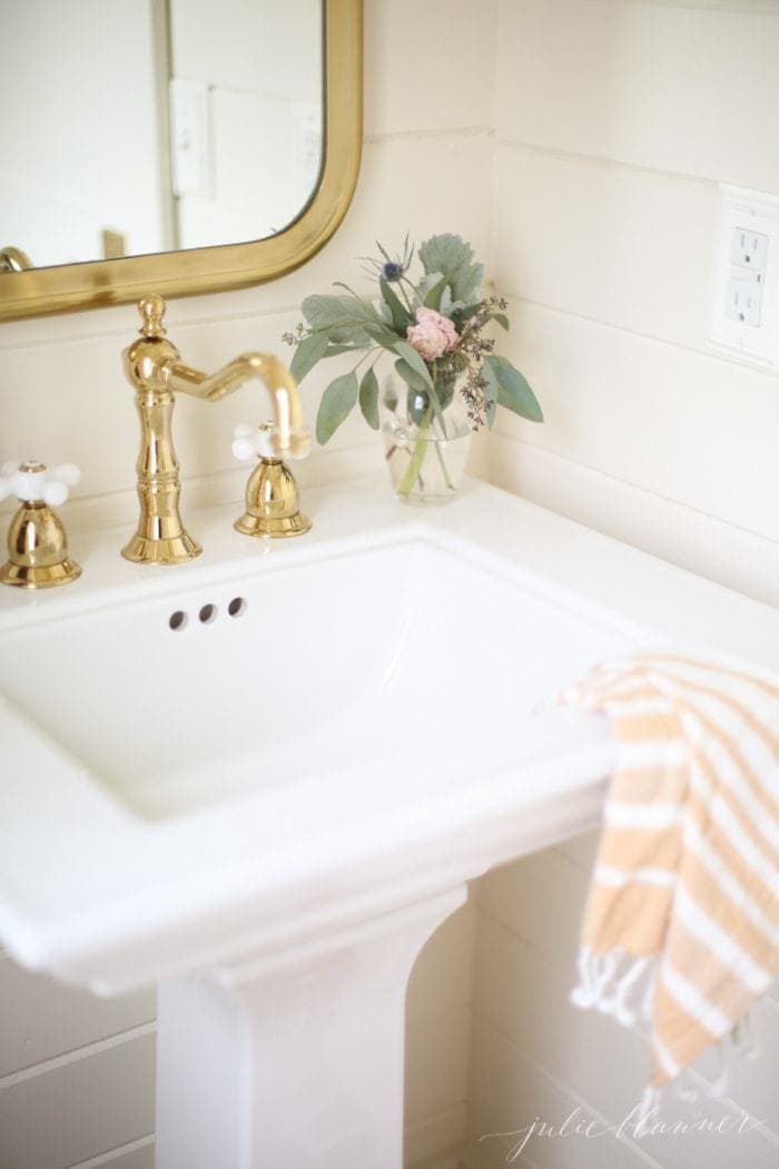 A white bathroom sink with gold faucet and mirror above.