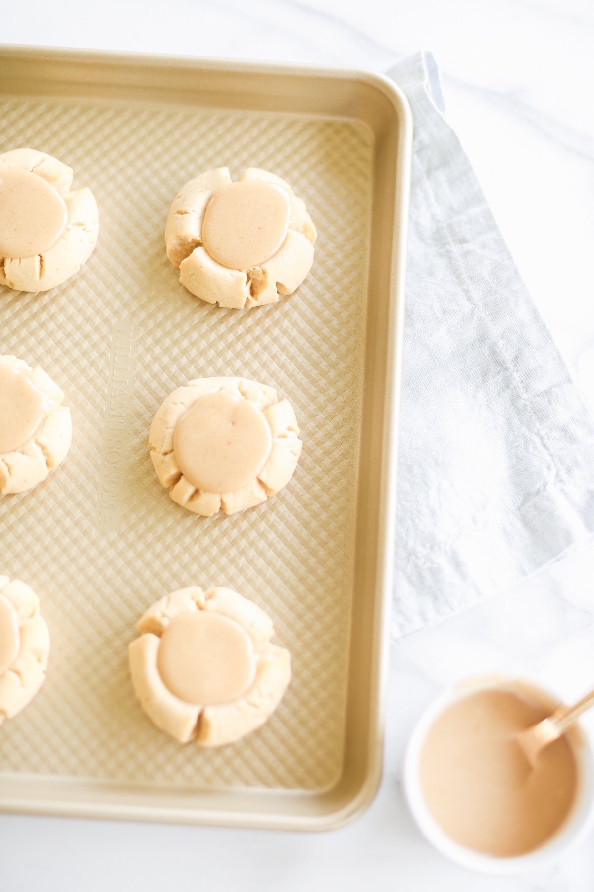 Caramel peanut butter cookies on a baking sheet next to a bowl of peanut butter.