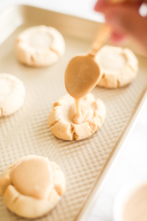 A person is drizzling **caramel** over **cookies** on a baking sheet.