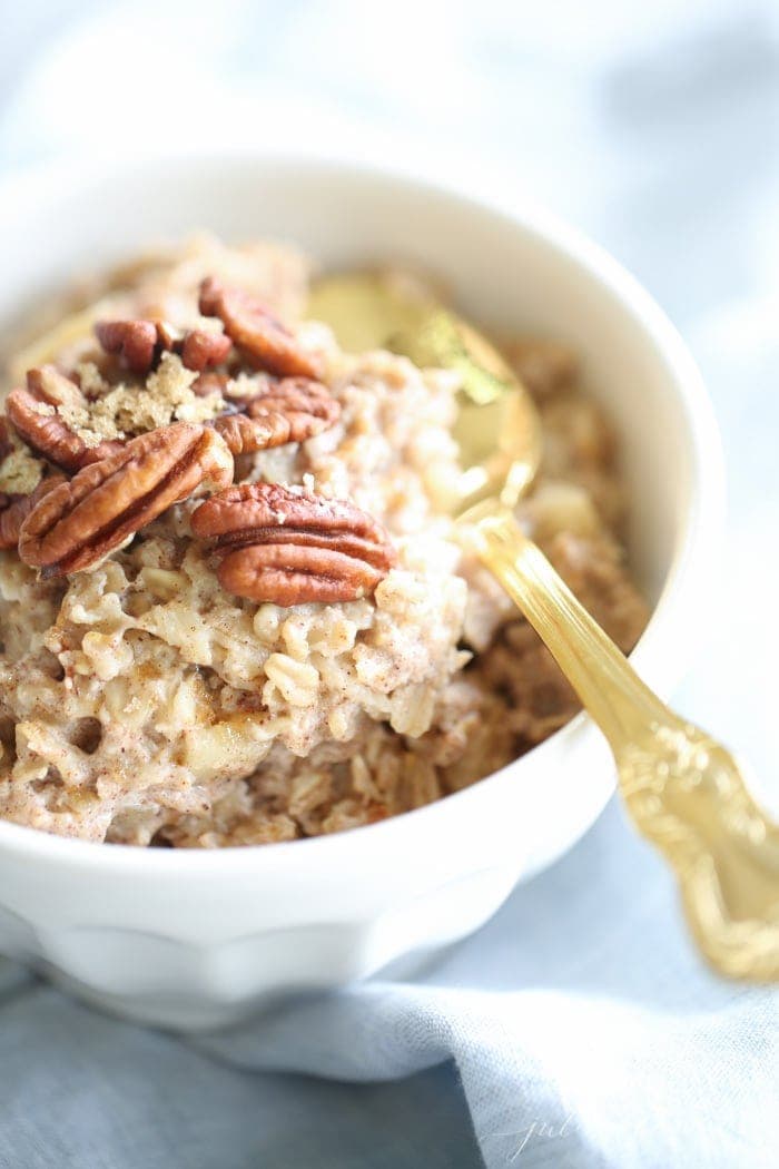 apple pie oatmeal in a white bowl with a gold spoon