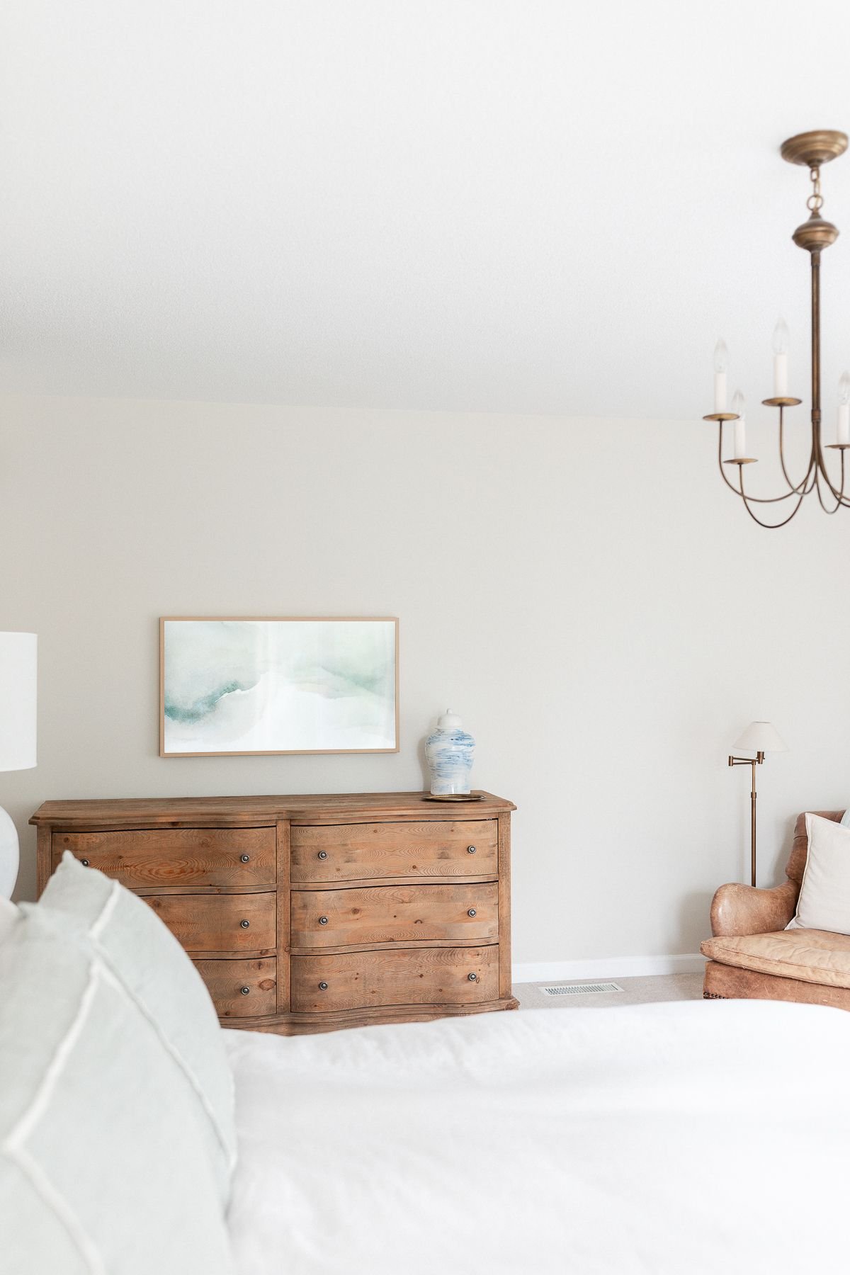 A bedroom with a wood dresser and neutral paint color on the walls