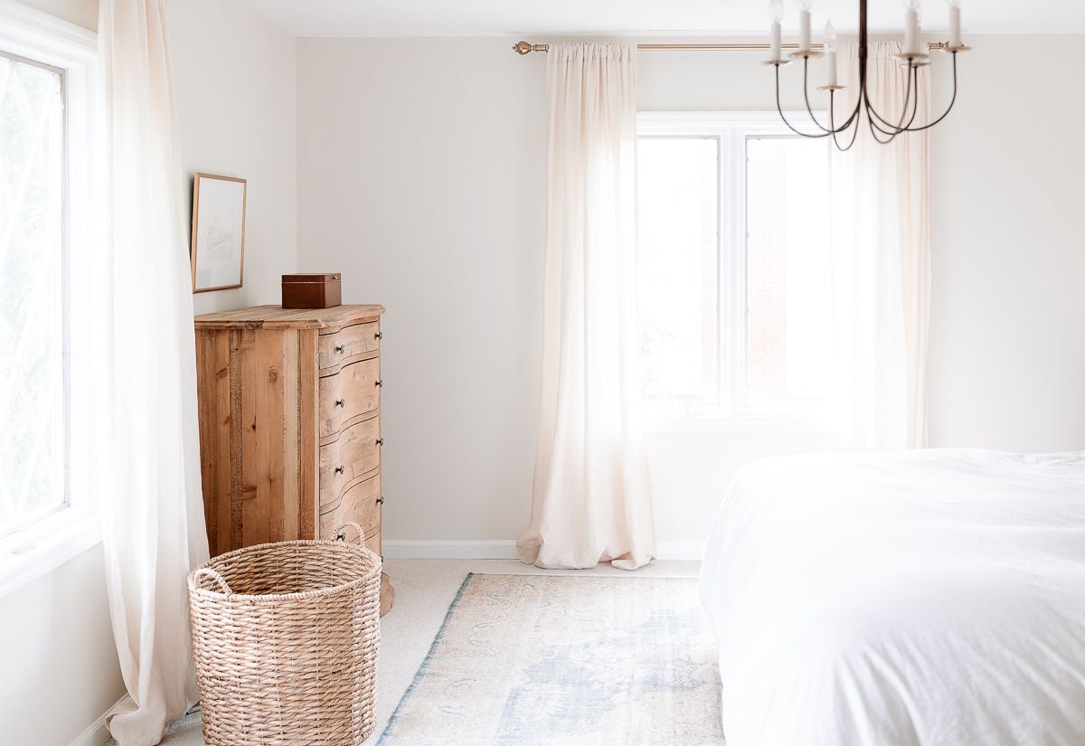 A bedroom with a wood dresser and neutral paint color on the walls