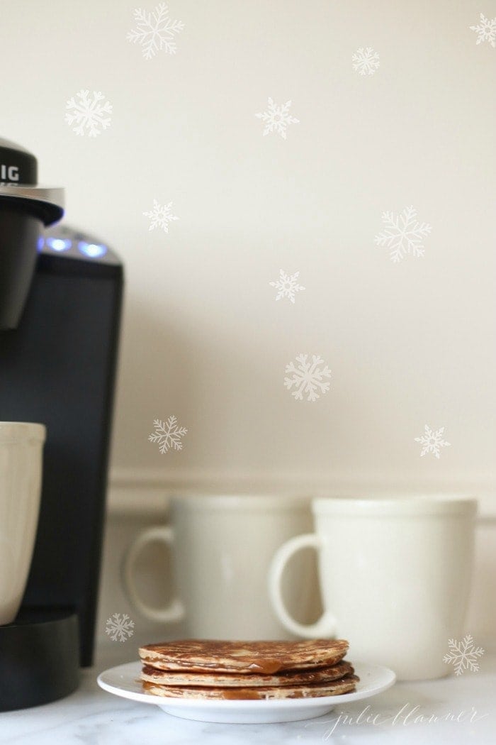 A coffee maker, two white mugs and a plate of stroopwafels