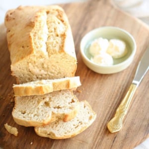 A loaf of honey beer bread with butter on a wooden cutting board.