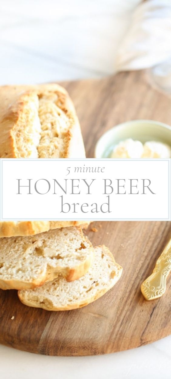 Loaf of partially sliced honey beer bread on a wooden board with a ramekin of butter next to it.