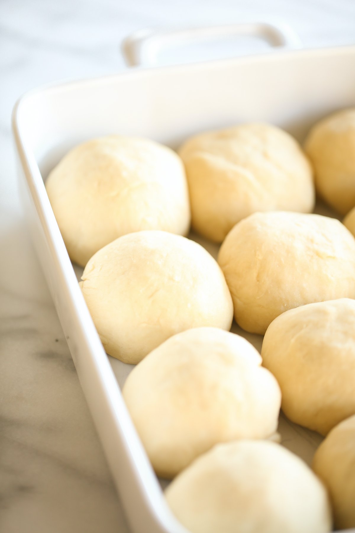 A white baking pan full of homemade dinner rolls before they go in the oven.