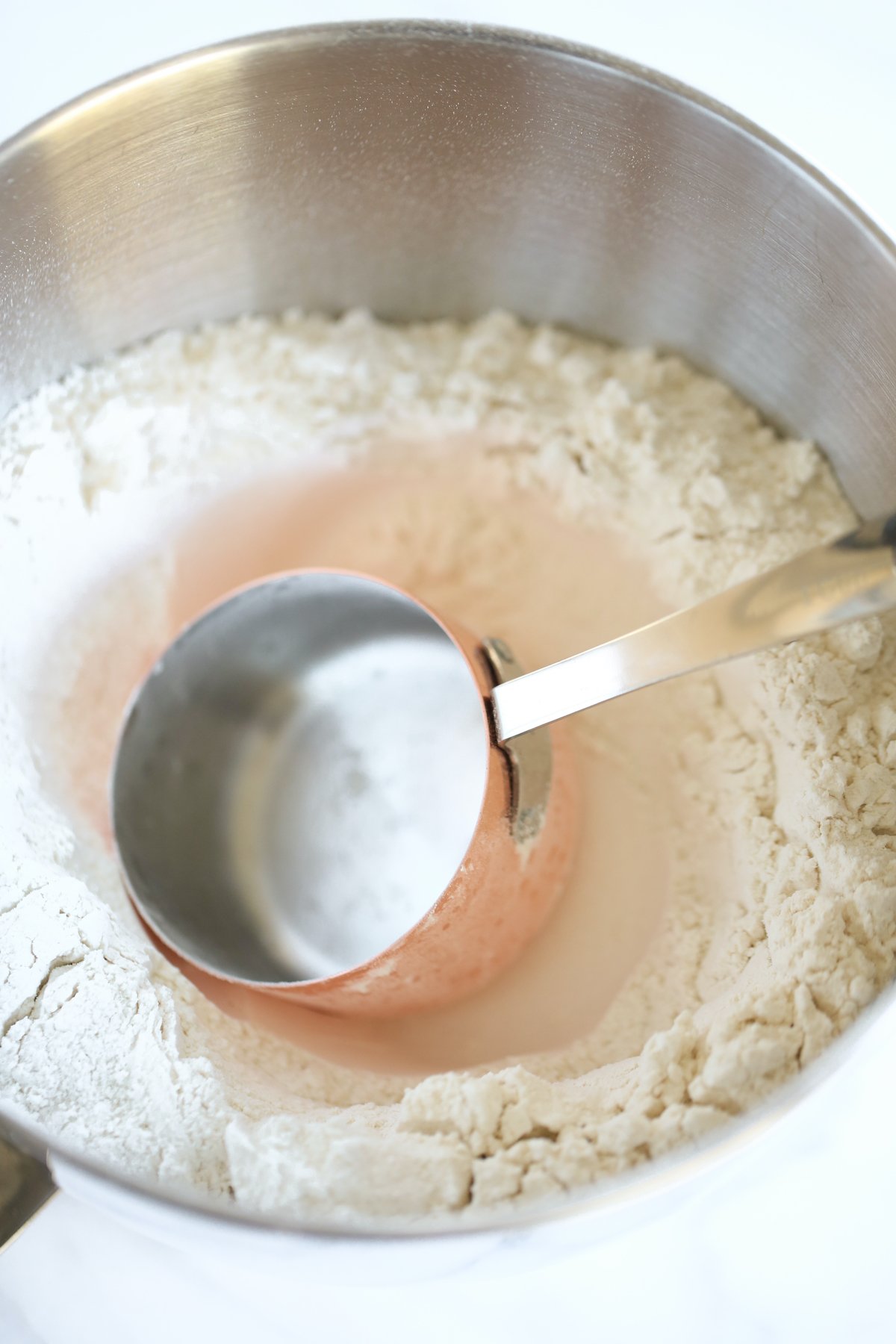 Flour inside a stainless steel bowl, with a measuring cup inside the flour.