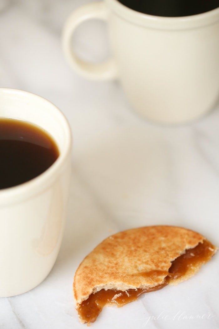 a stroopwafel with bites taken out, 2 cups of coffee in the background