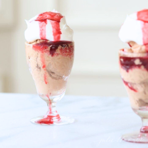 A delightful dessert featuring two glasses of rich chocolate mousse topped with whipped cream and raspberry sauce.