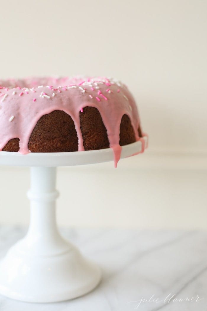 pink glazed donut cake with sprinkles on a white cake stand