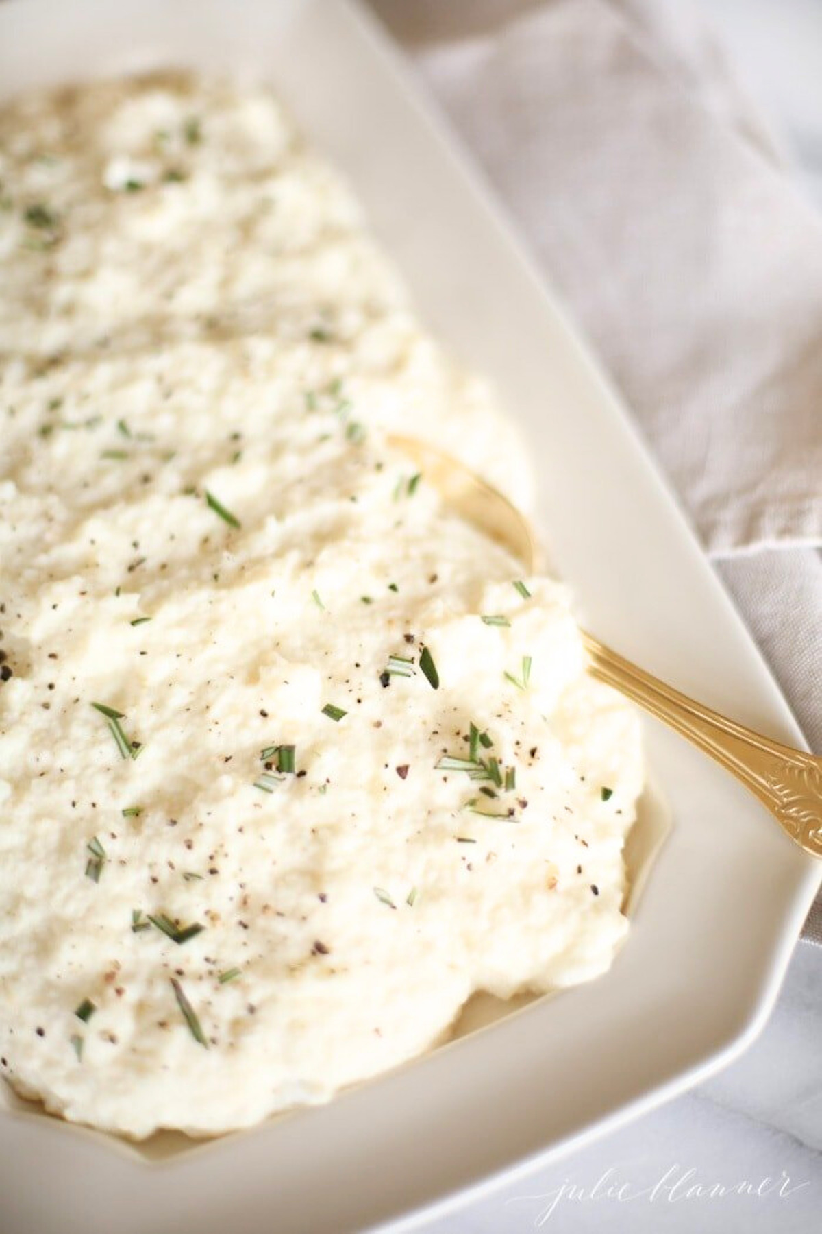 White risotto with cauliflower mashed potatoes on a white plate with a gold spoon.