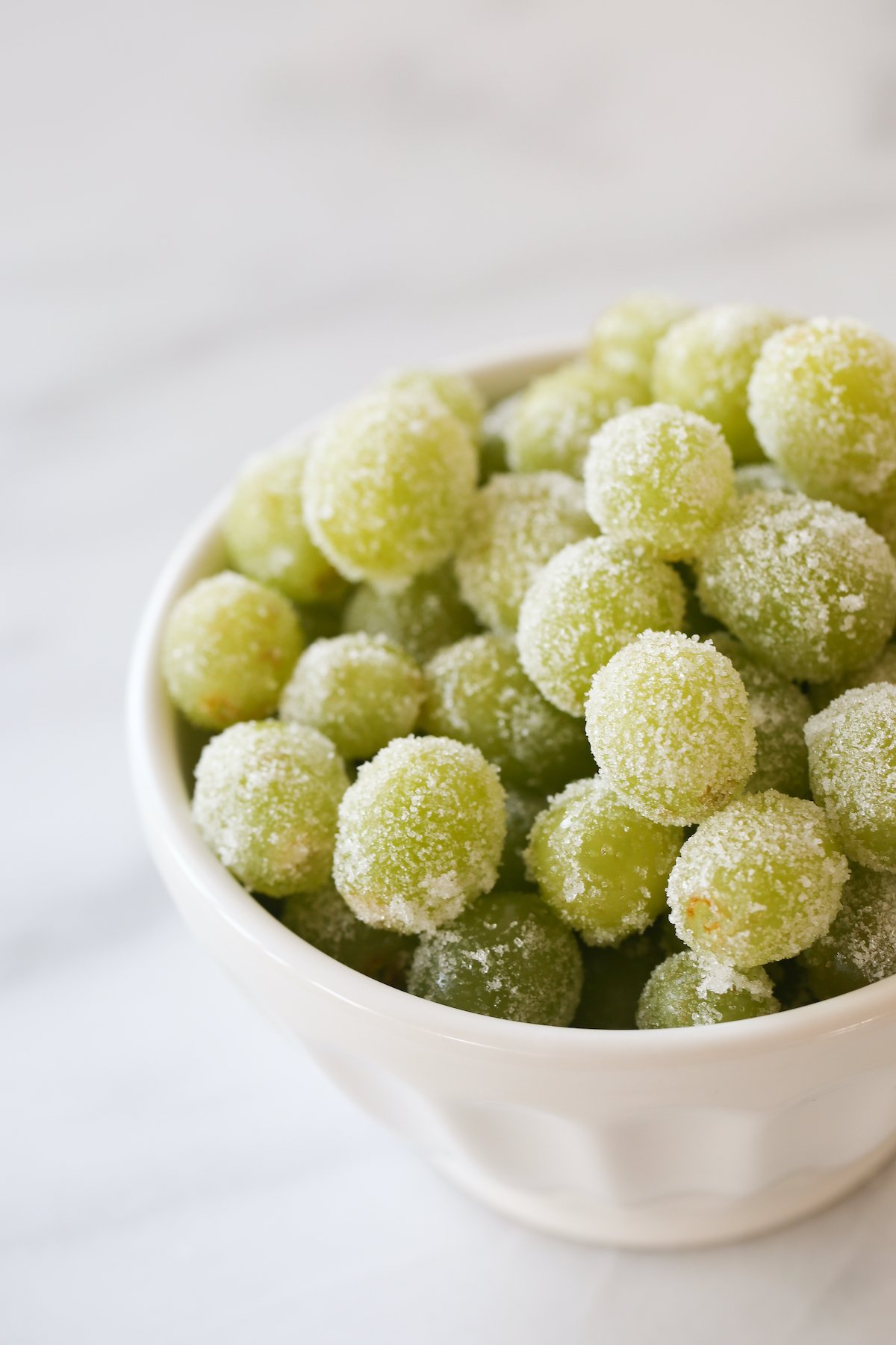 A white bowl of green sugared champagne grapes.