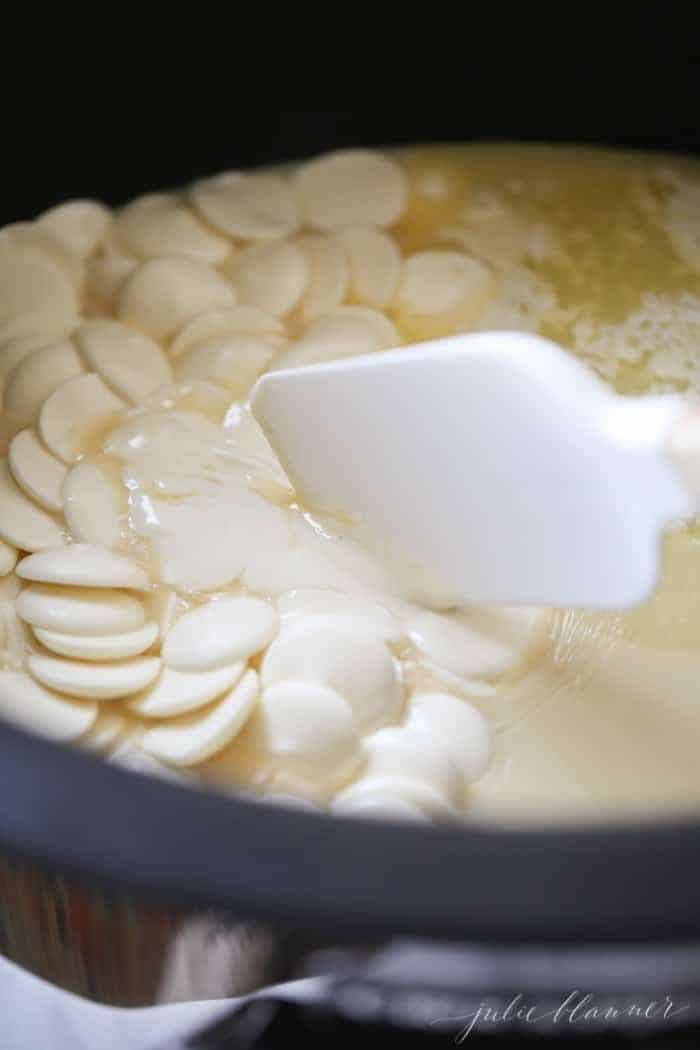 Crockpot fudge in the making, with melted white chocolate fudge inside, spatula stirring.