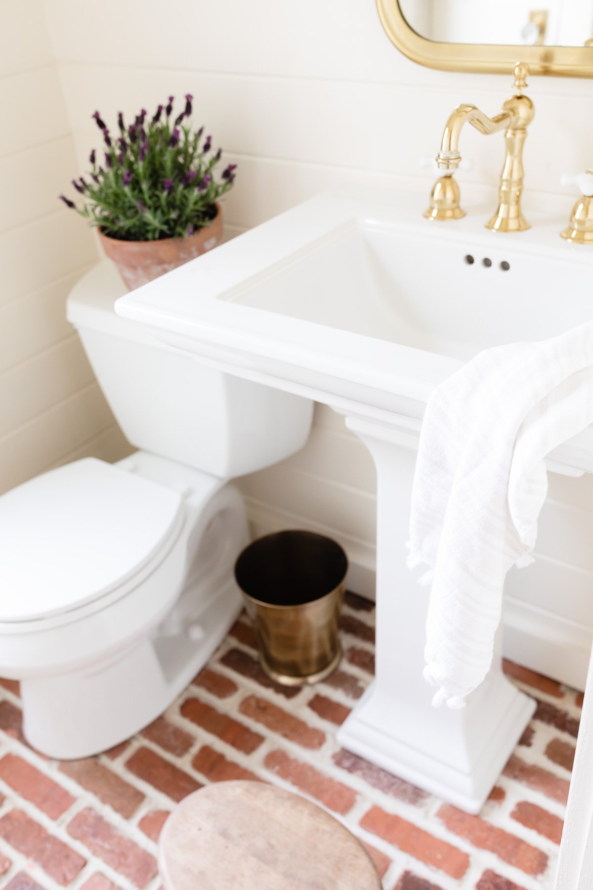 A small bathroom with a pedestal sink and brick flooring.