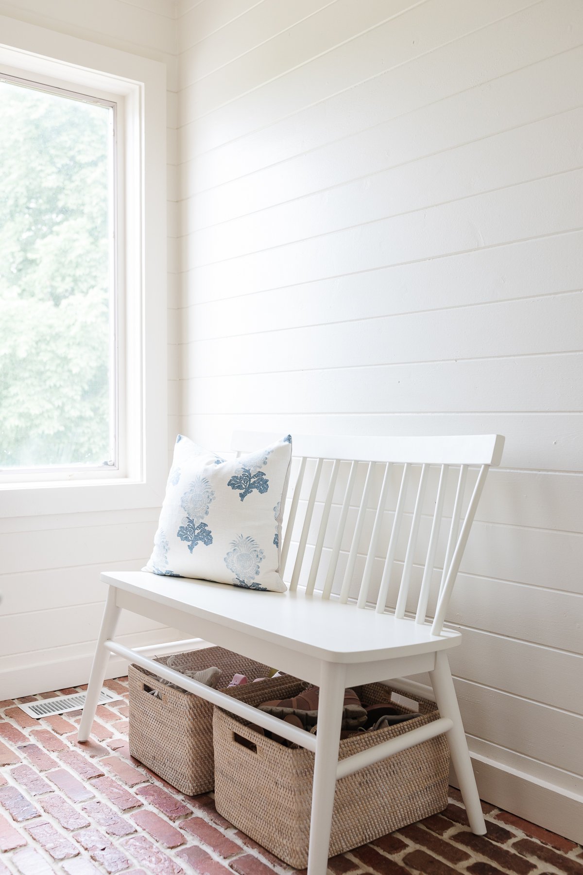 A mudroom with white wood paneled walls and brick flooring.