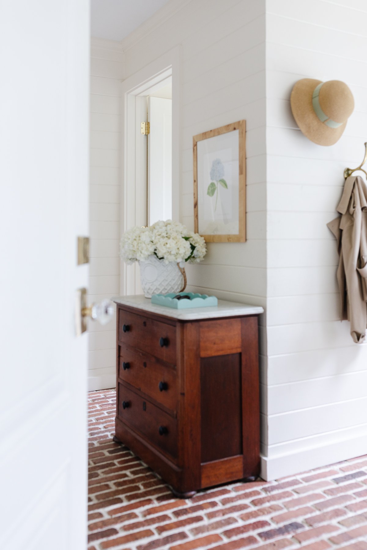 A mudroom with white wood paneled walls and brick flooring.