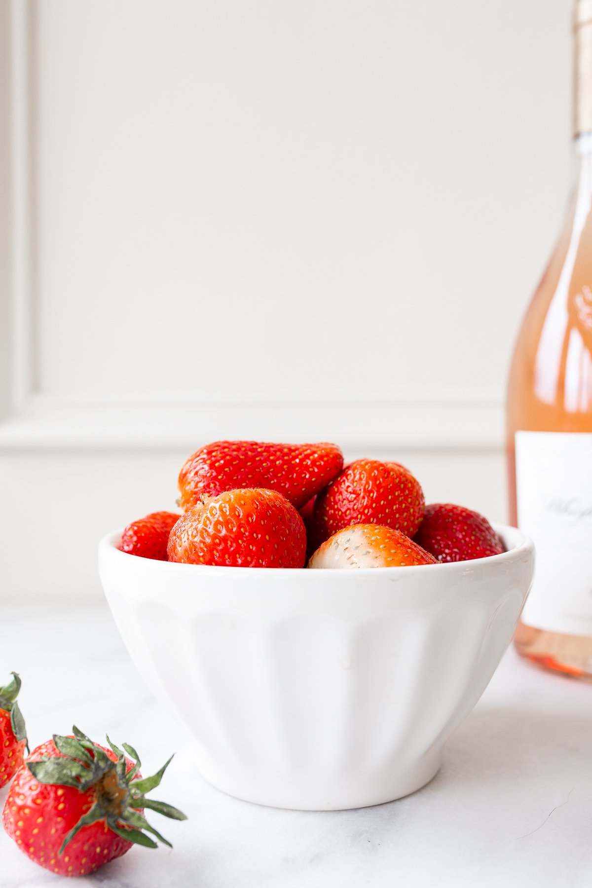 rosé marinated drunken strawberries in a white bowl, bottle of wine in the background.