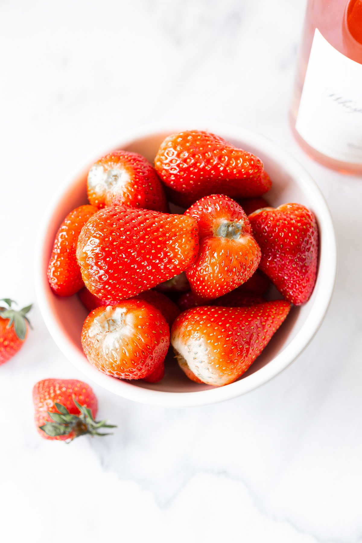 rosé marinated drunken strawberries in a white bowl, bottle of wine in the background.