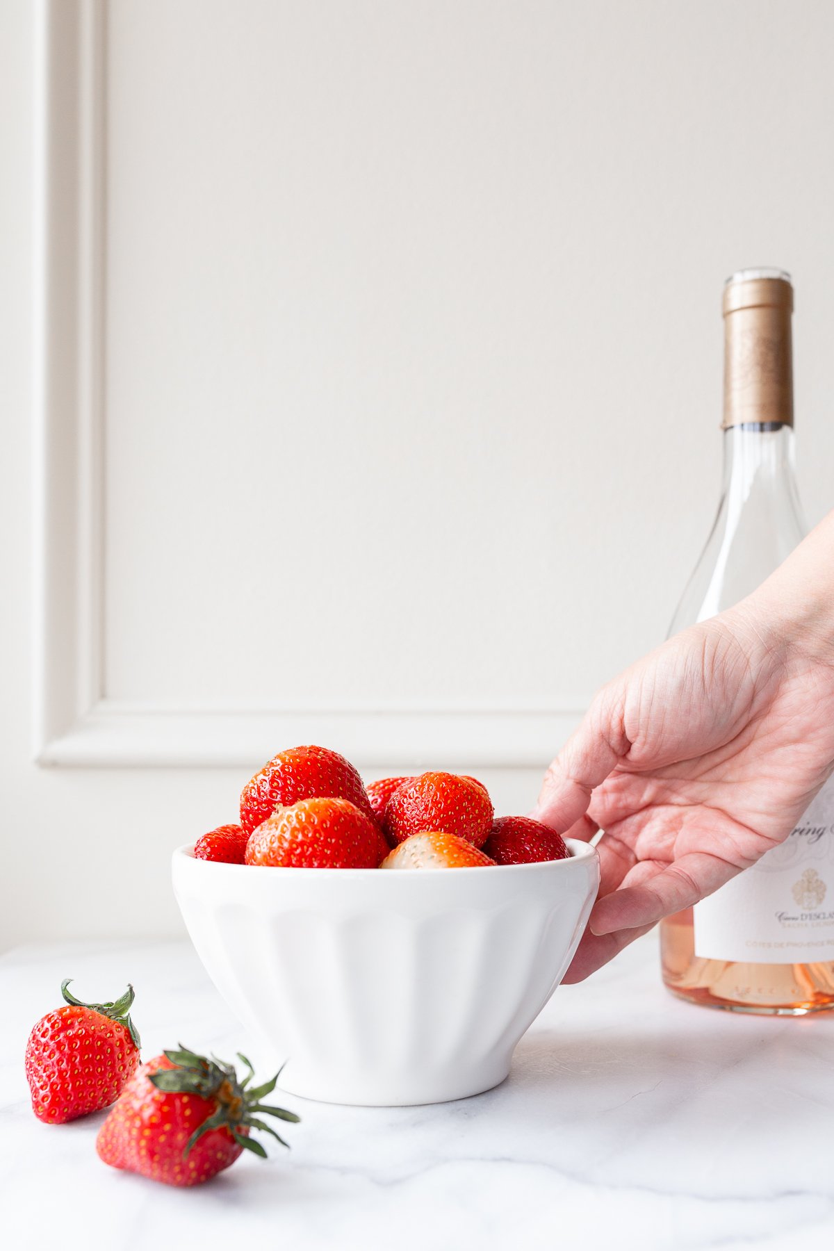 rosé marinated drunken strawberries in a white bowl, bottle of wine in the background.