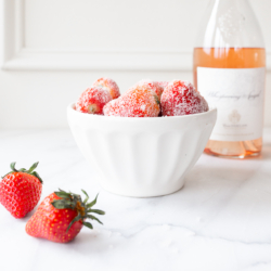 rosé marinated drunken strawberries in a white bowl, bottle of wine in the background.