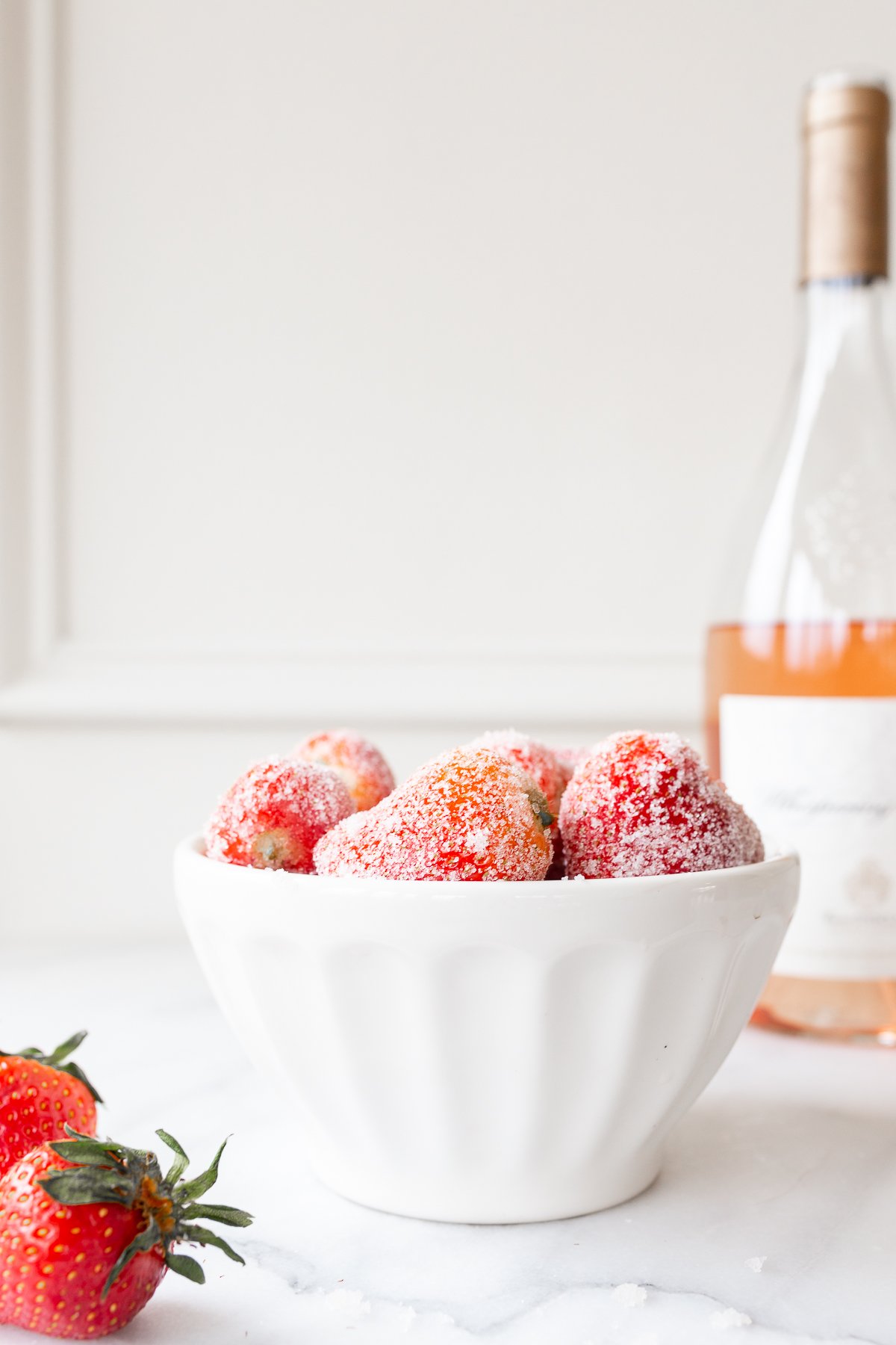 rosé marinated drunken strawberries in a white bowl, bottle of wine in the background.