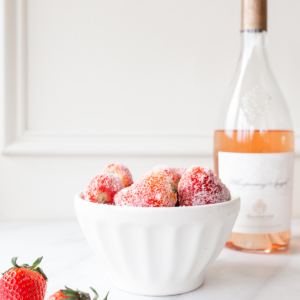 rosé marinated drunken strawberries in a white bowl, bottle of wine in the background.