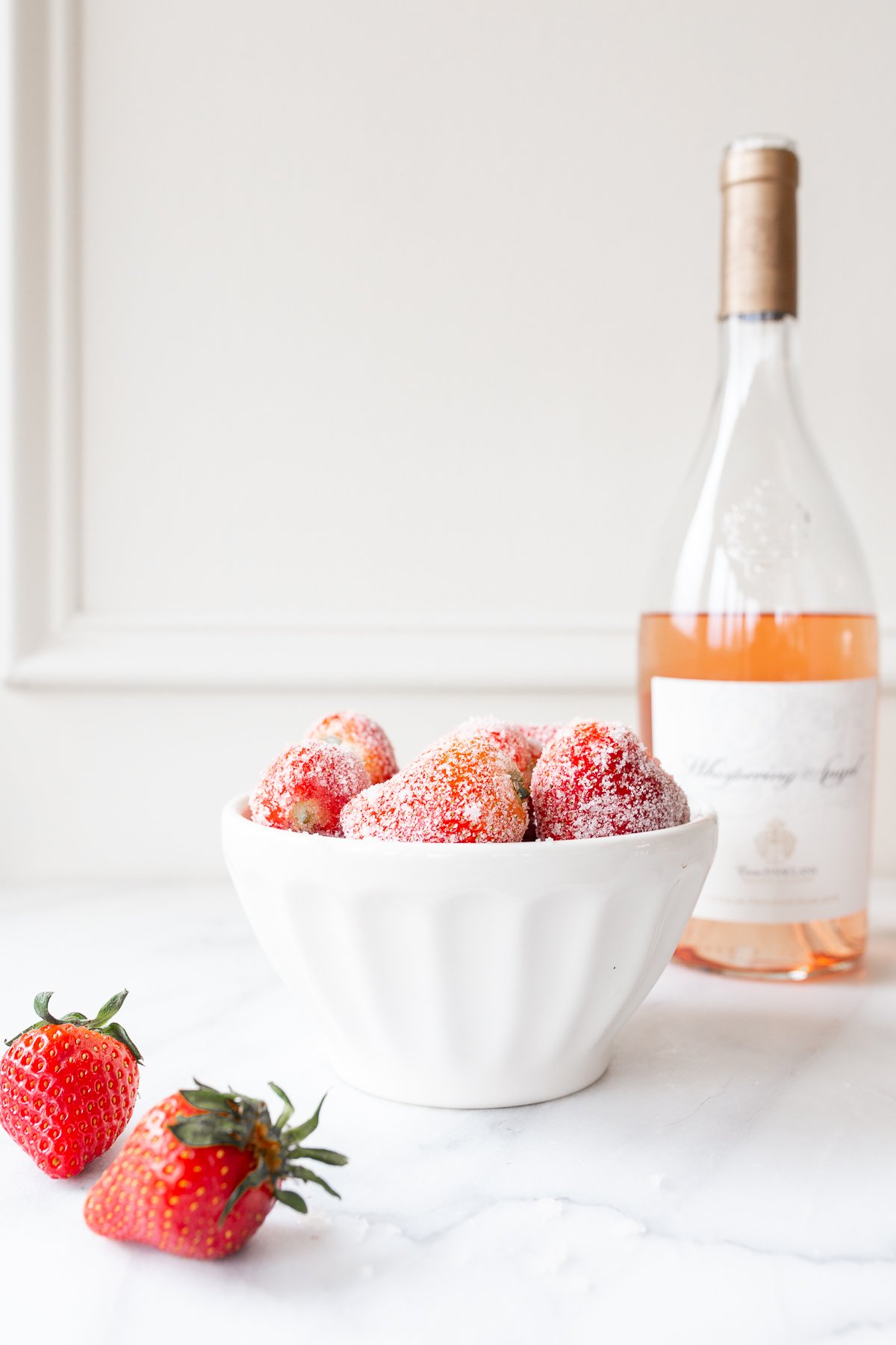 rosé marinated drunken strawberries in a white bowl, bottle of wine in the background.