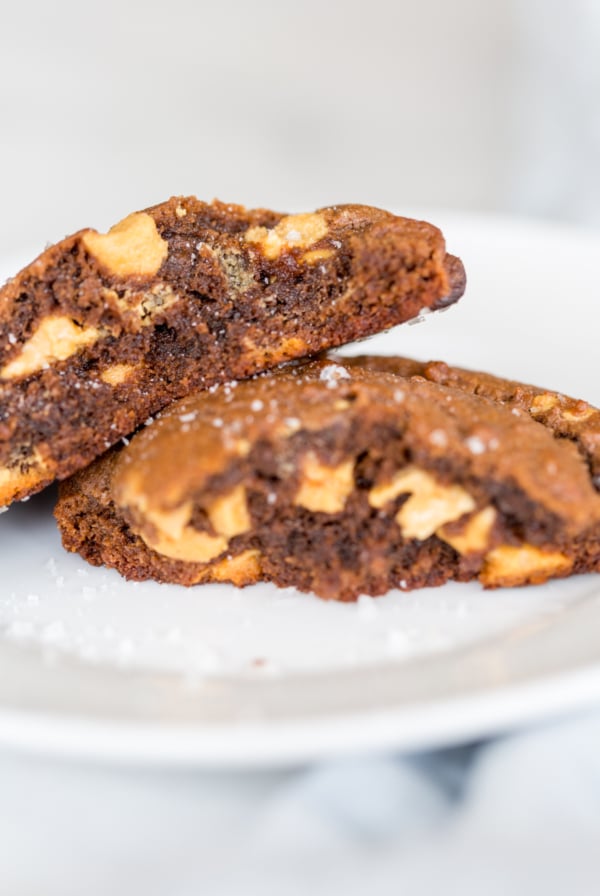 A chocolate cookie with peanut butter chips, split in half on a white plate.