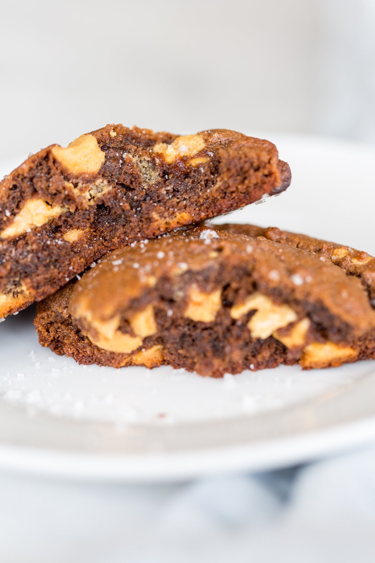 A chocolate cookie with peanut butter chips, split in half on a white plate.