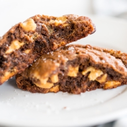 A chocolate cookie with peanut butter chips, split in half on a white plate.