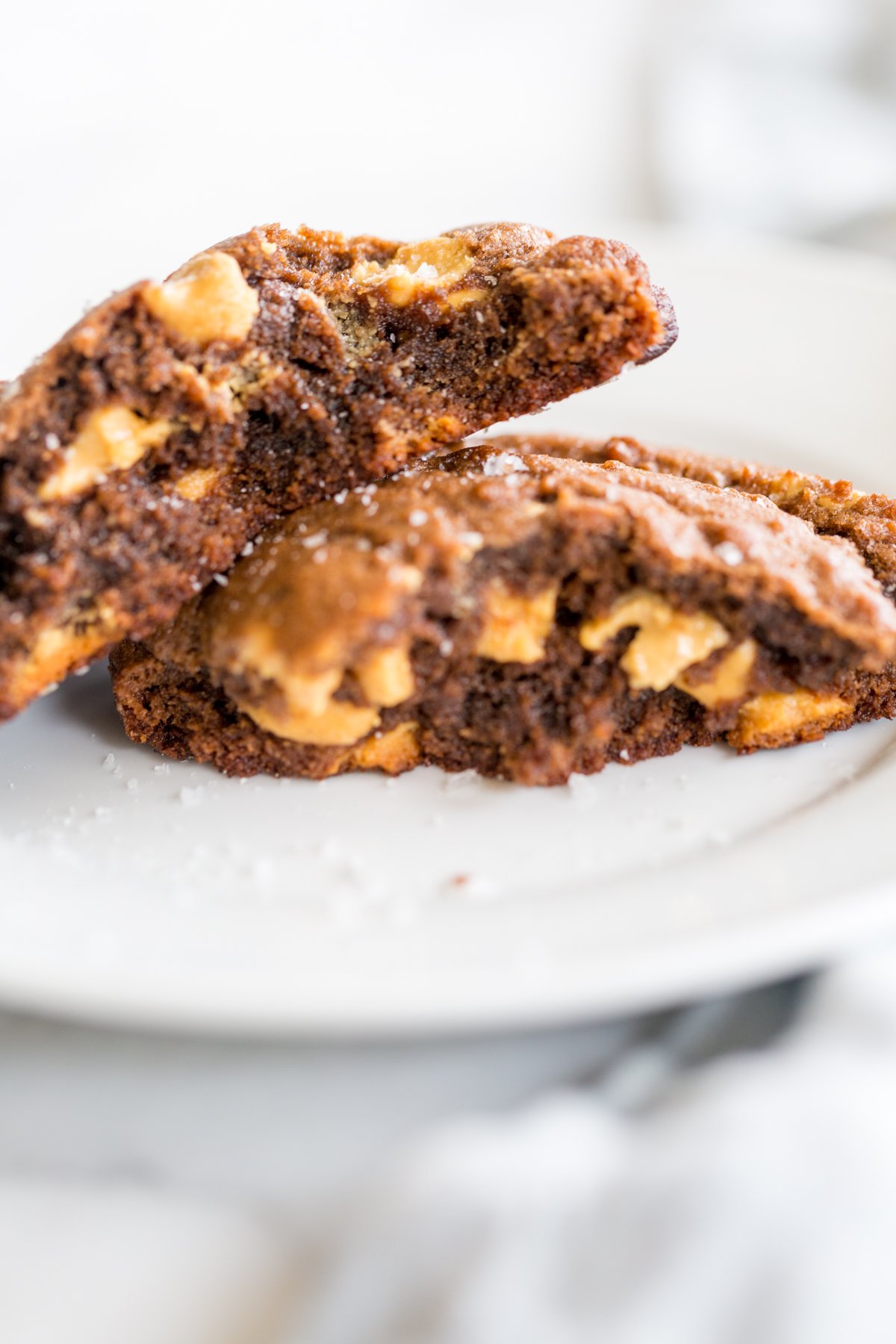 A chocolate cookie with peanut butter chips, split in half on a white plate. 