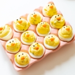 Deviled eggs made into little Easter chicks, on a pink ceramic egg holder.